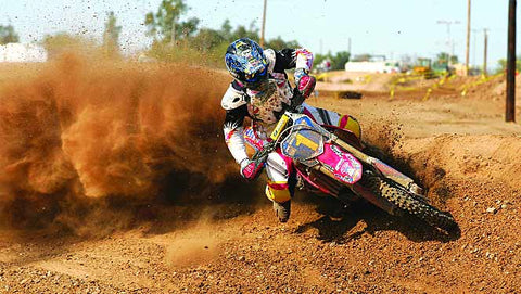 Rider exiting a corner. Rider is bring the inside foot back to the peg and coming back on the throttle to exit the corner. Dirt is flying behind the rear wheel as the rider gets on the gas.