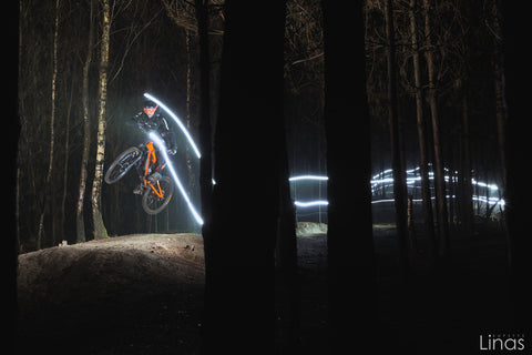 Mountain biker going through the woods. with a light mounted to their head and to the handlebars of the motorcycle. The picture shows the light array of where the rider has been.