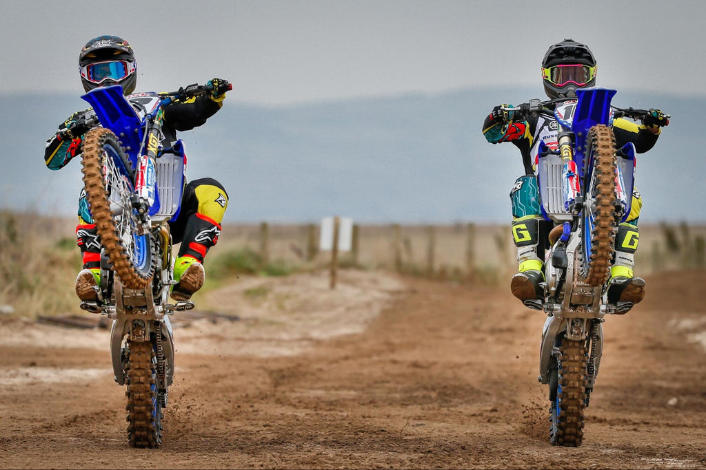 two risk racing pro riders wheelieing high up directly at camera