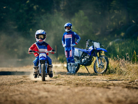 Young motocross rider learning to ride on the appropriately sized motorcycle. The height and power output is well suited for the riders abilities. The young rider is learning to ride as a parent watches and instructs them.