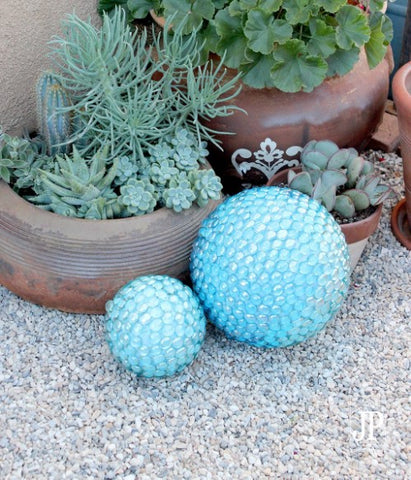 Garden orbs covered in blue glass beads sit in a rocky, outdoor area.