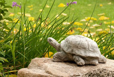 A stone sculpture of a turtle sits atop a rock in a grassy, flowered field. 