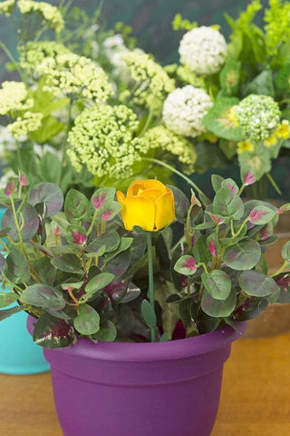 A yellow rose plant pick is staked into a potted plant.