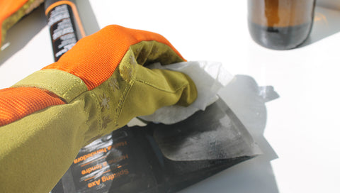 person rubbing oil onto an axe blade wearing gardening gloves