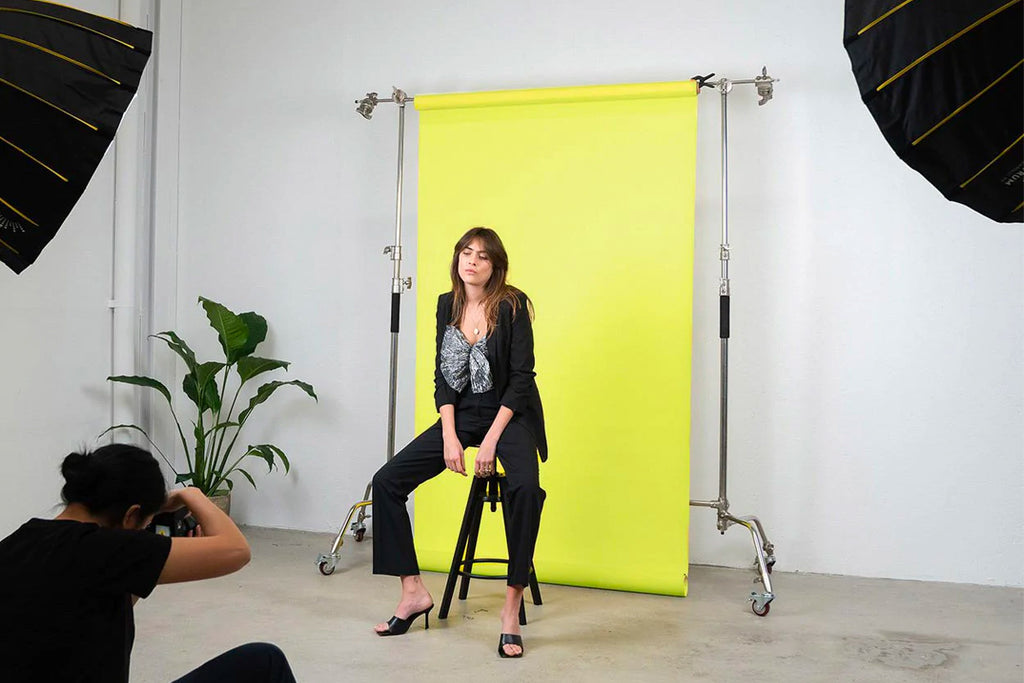 Female model sitting in front of a yellow backdrop while photographer takes photos of her