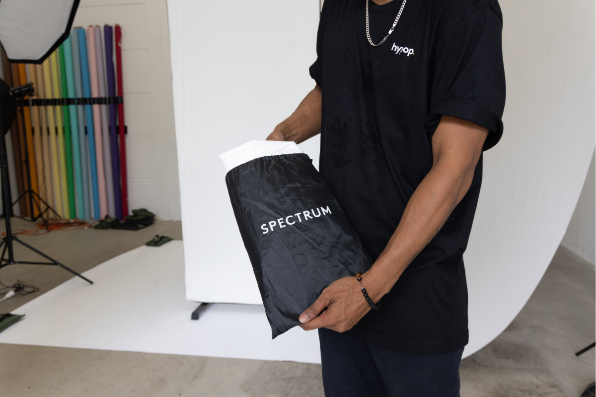 a male photographer setting up the studio holding a spectrum black bag in front of a white backdrop.