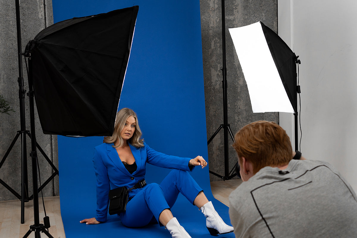 a photo of a male photographer taking a photo of a fashion model in a blue suit on a blue backdrop with a two-point lighting setup.