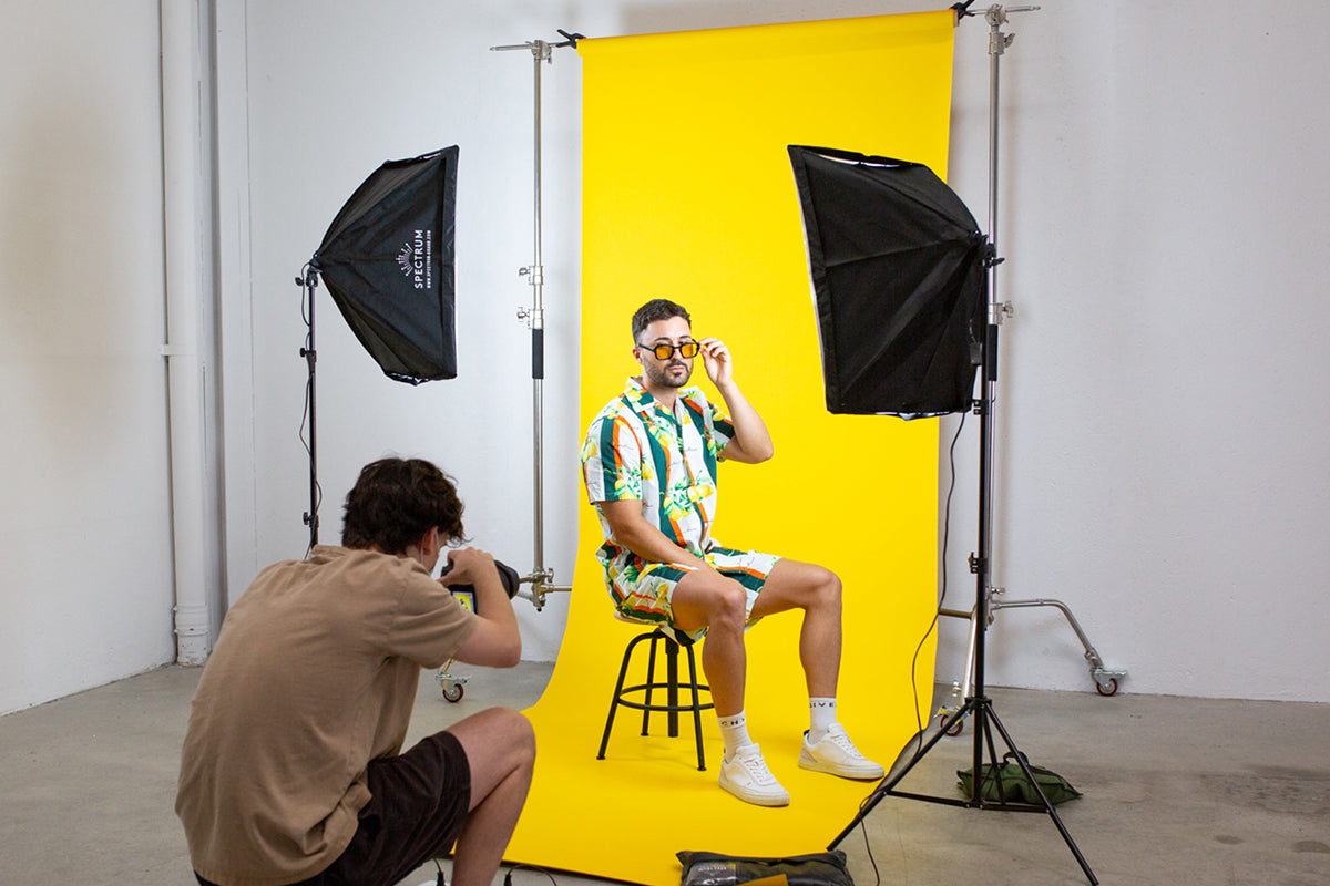 image of a photographer taking a photo of a fashion model in front of a yellow backdrop with a two-pint lighting setup.