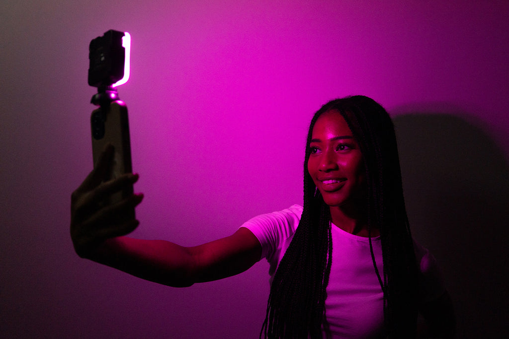 Woman taking a selfie on her phone which is being lit up with a pink hue from a photography light