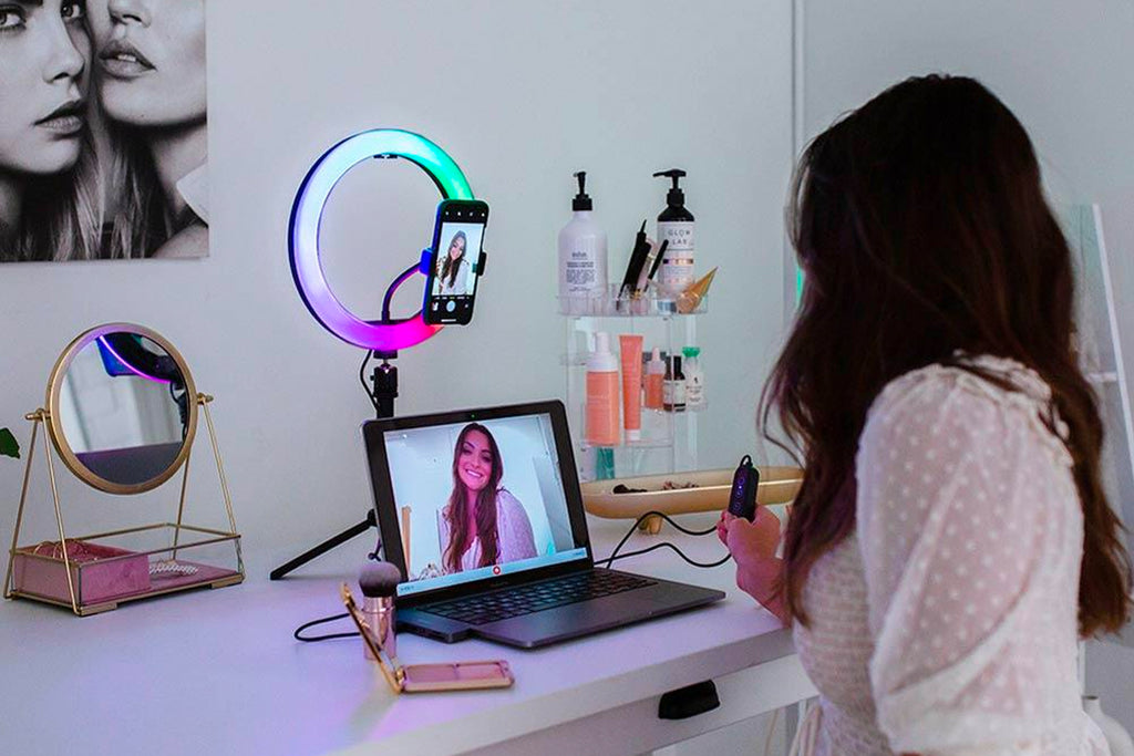 Woman smiling at a desk using a ring light which is behind a laptop