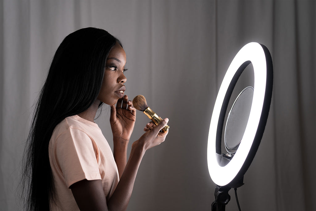 Female holding a makeup brush and looking at a mirror attached to a ring light