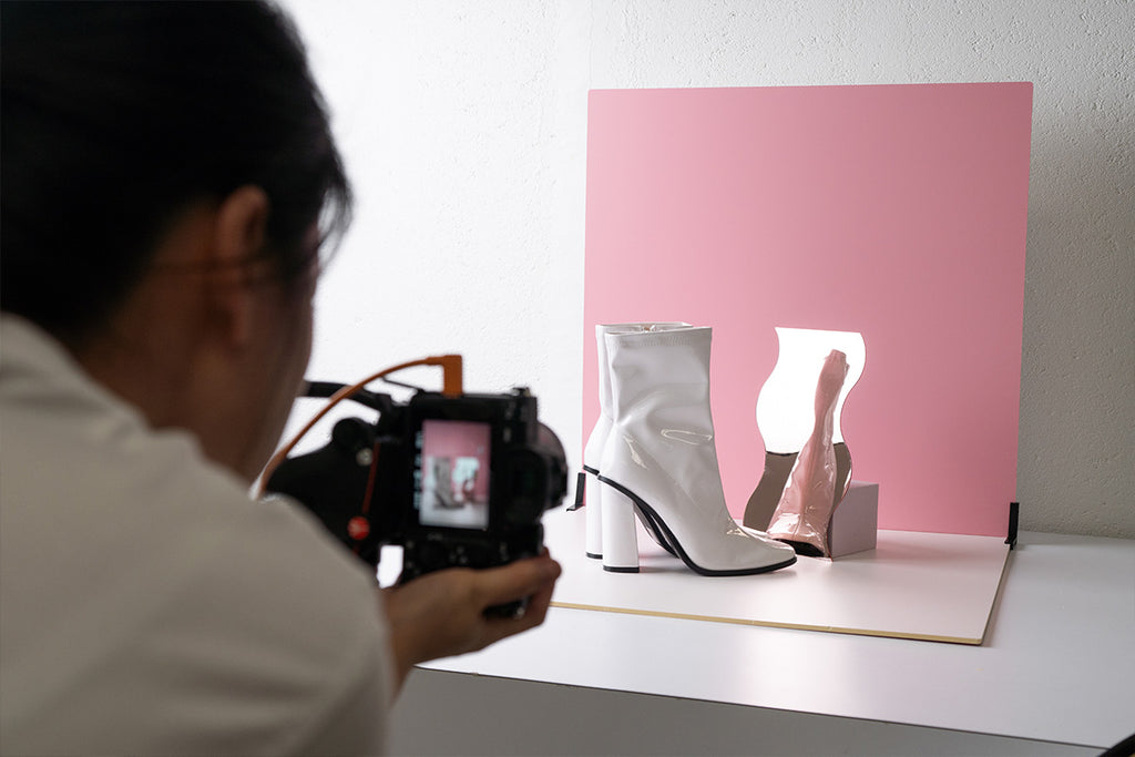 Photographer taking photos of white shoes on a pink backdrop