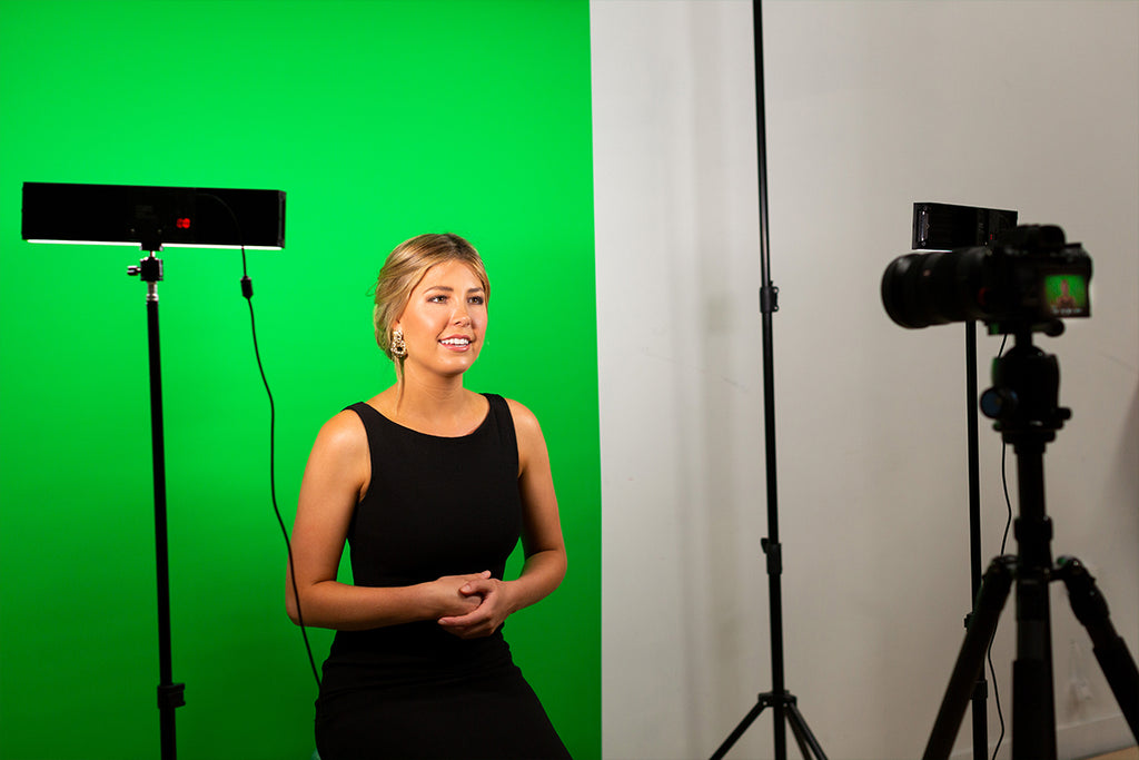 Woman recording herself on a camera and sitting in front of a green backdrop with two LED lights