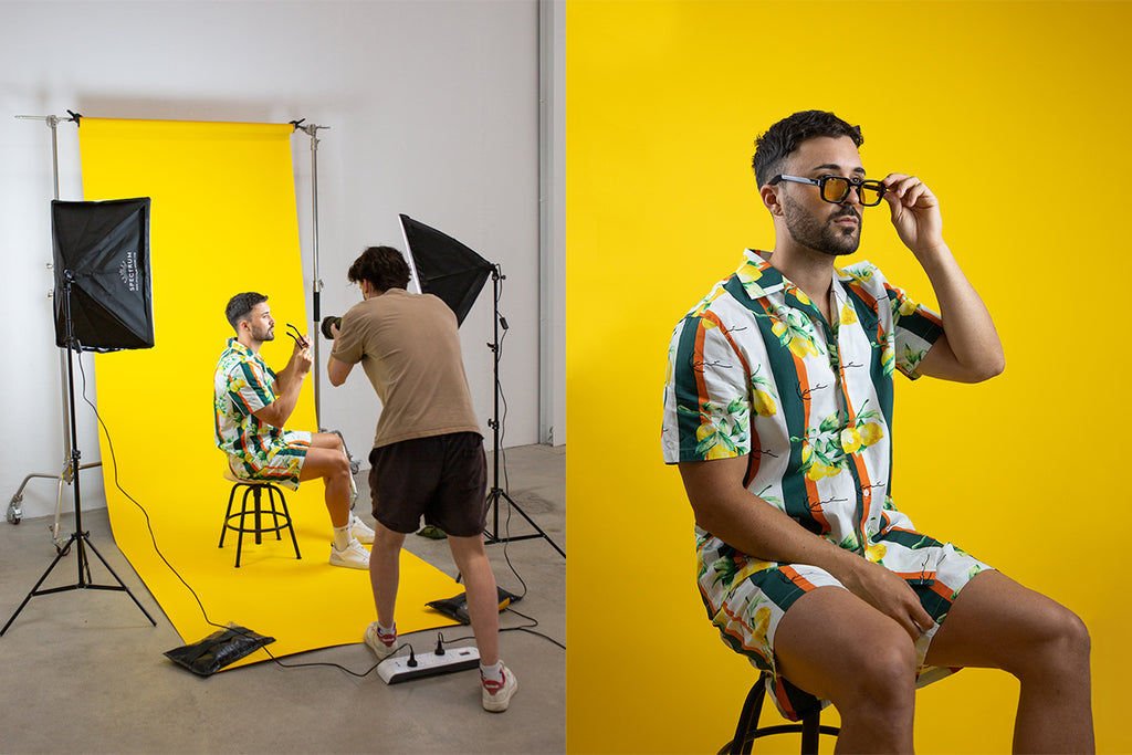 Two images. First image: Male photographer taking photos of a male model sitting in front of a yellow backdrop. Second image: Male model sitting in front of yellow backdrop