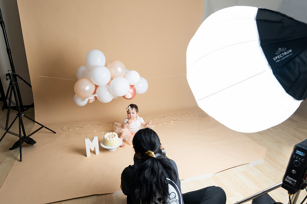 Female photographer taking a photo of a baby in front of a brown backdrop with balloons  