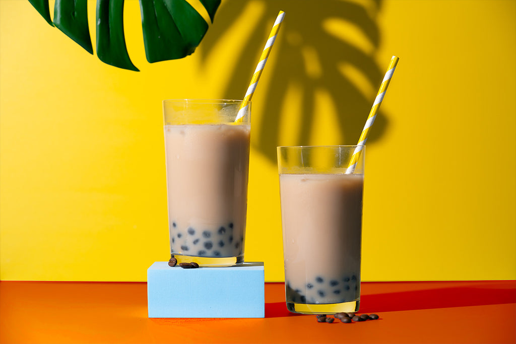 Two bubble teas positioned in front of a yellow backdrop