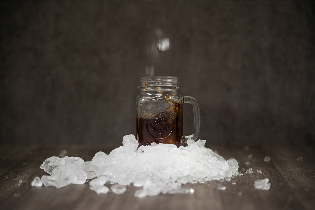 Coffee in a glass jar surrounded by ice positioned on a dark wooden backdrop