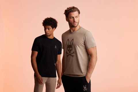 fond orange avec deux gars debout, l'un devant avec un tee-shirt beige et l'autre avec un tee-shirt noir