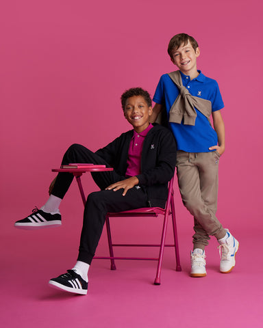 deux enfants sur fond fushia, l'un est assis et l'autre debout tous les deux souriants