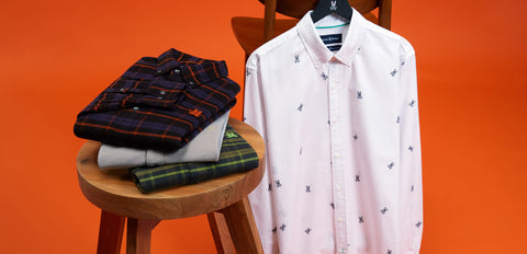 image of a Psycho bunny white shirt hanging and some polos staged on a chair with an orange background