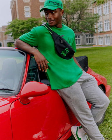 A man leaning against a red car wearing Psycho Bunny