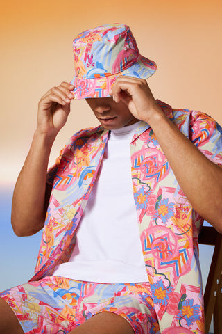man wearing a bucket hat, a shirt and a swim with the same matching pattern, sitting on a  chair