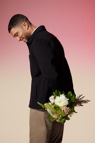 man standing with a dark jacket and a bouquet of flowers in his hands