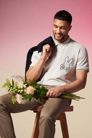 men sitting down on a pink background with flowers in his hand