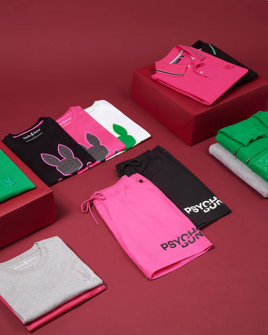 ropa de neón doblada en rosa, verde, negro, gris y negro de psycho bunny sobre un fondo burdeos