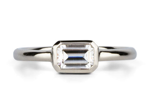 Bezel Set ring with an emerald cut moissanite in white gold