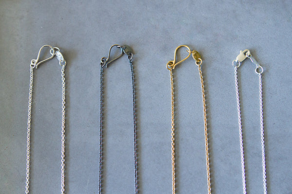 Close the clasp on your necklaces to avoid tangles. Four necklaces with hooked clasps in a row.