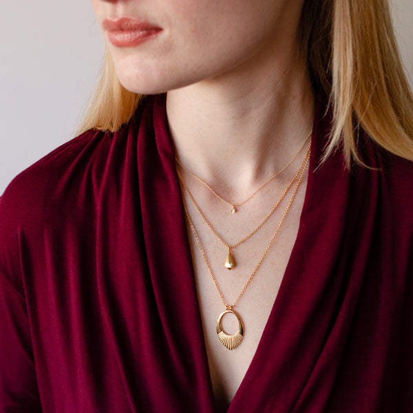 Three vermeil necklaces layered on the neck of a model wearing a maroon wrap top