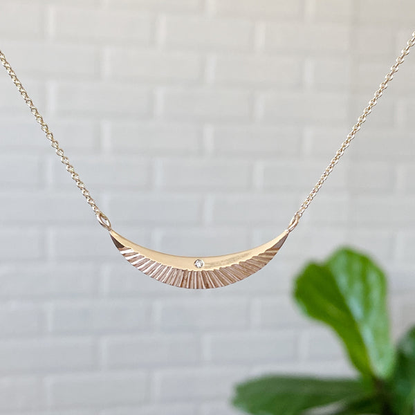 gold textured crescent necklace with a single diamond in the center and carved rays