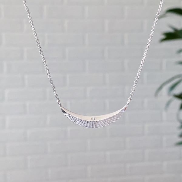 Silver icarus crescent necklace with a diamond hanging in front of a white wall