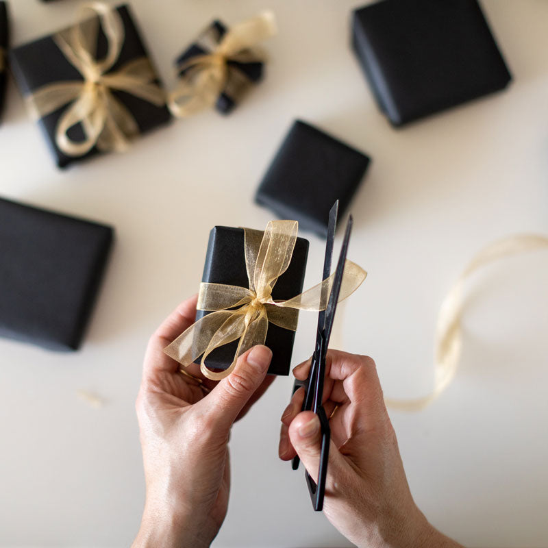 Gift wrapping a jewelry box with one hand cutting a gold ribbon with scissors