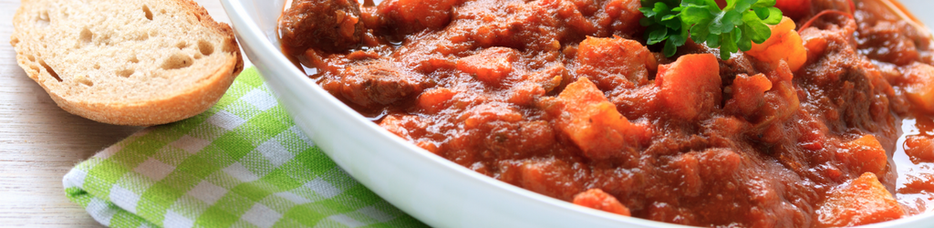 Hearty Vegetable Goulash on a table with a checkered green and white napkin and a slice of rustic bread.