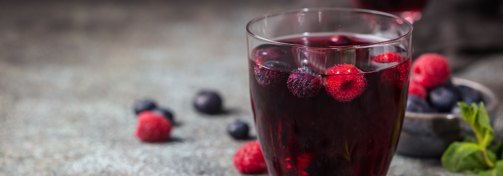 Glass of red wine with mixed berries. Background: berries and sprigs of mint.