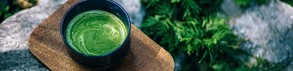 a cup of matcha tea on a wooden board with a nature background.