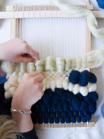 This is an overhead picture of a woven wallhanging being made on a small frame loom. The maker is creating a looped texture with gold lurex roving.