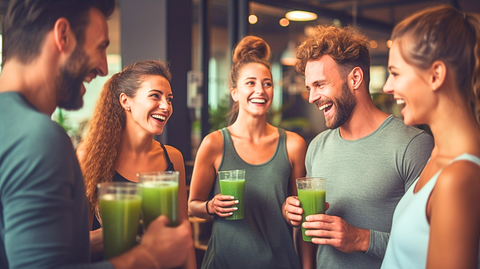 A group of friends in workout attire engages in lively conversations and enjoyment while savoring their green juice within the gym.