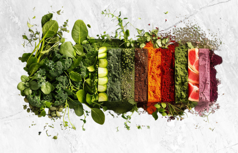 A horizontal line-up of different ingredients found in super greens powders making a colorful array of superfoods and herbs.
