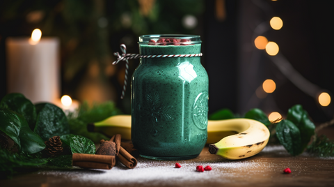 A glass of rich dark green smoothie rests upon the table, surrounded by ripe bananas and sticks of fragrant cinnamon bark, set against a festive Holiday-themed background.