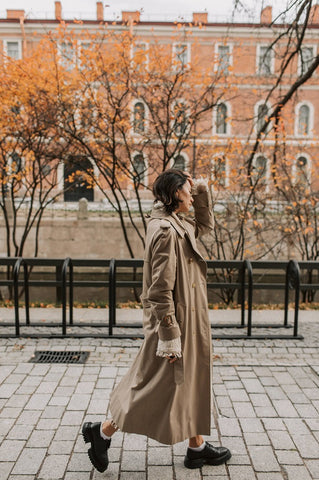 Woman wearing fall layers to protect skin from eczema and anti-aging benefits walking on the city street in the fall by pure and coco