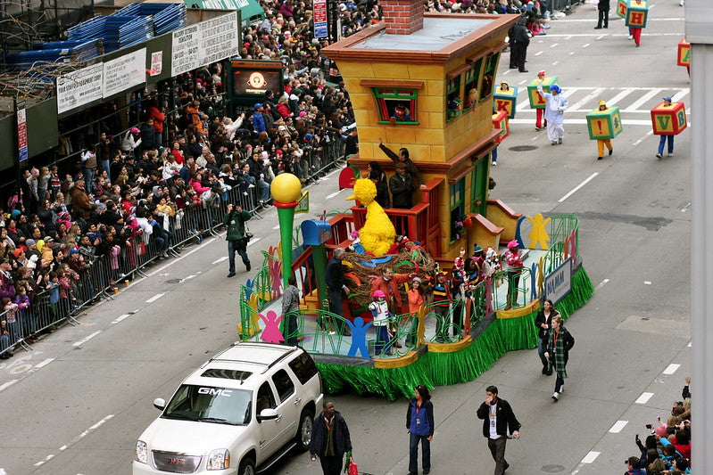 Bird's eye view of a parade float making its way through the Macy's Thanksgiving Parade as large crowds look on and cheer.