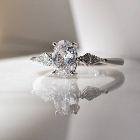 A stunning Oval Cut Diamond Ring with its reflection on a white shiny surface.