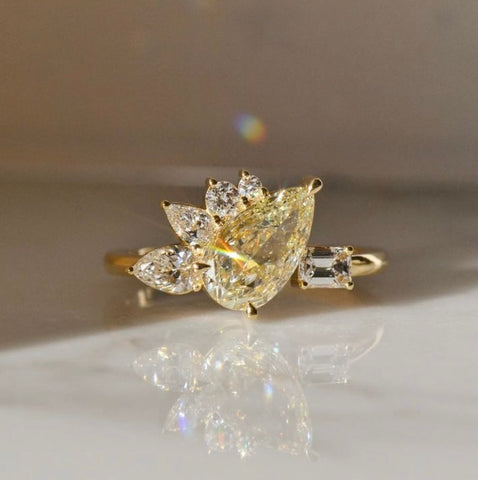 A pear cut one of a kind yellow diamond ring placed on a white shiny surface