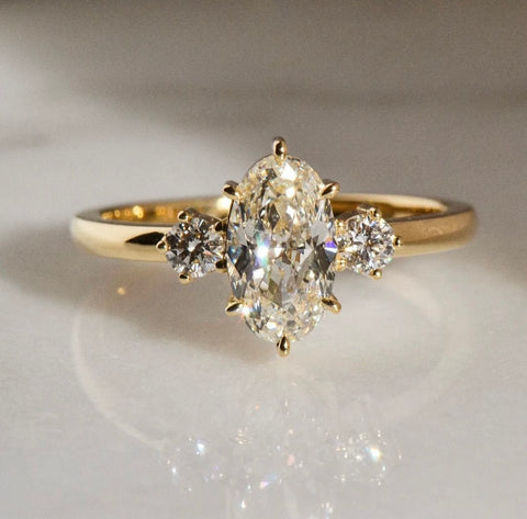 Vintage inspired three stone engagement ring featuring an oval cut white diamond and two round cut white diamond