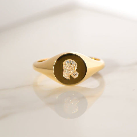 A revival women's gold signet ring placed on a white shiny surface