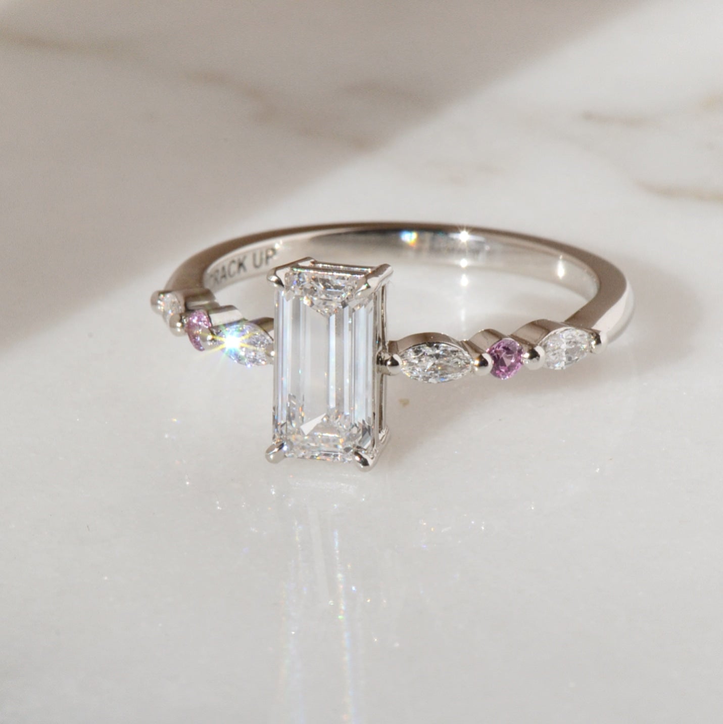 Elongated emerald cut engagement ring with marquise diamond and round pink sapphires along the band