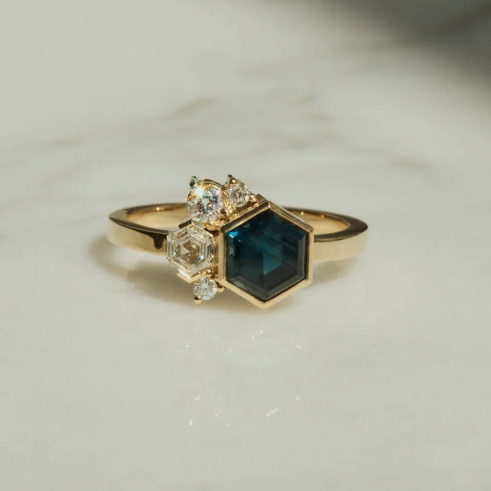 A hexagonal cut Australian sapphire bezel set centrally on a square band, accented by a hexagonal cut diamond, and a sprinkling of round cut diamonds; set in 18ct yellow gold